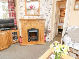A living room with a fireplace television flowers on a table and an armchair at The Retreat Near Shorwell