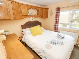 A bedroom with a double bed white bedding and yellow pillows wooden overhead cabinets and a window with curtains at The Retreat Near Shorwell