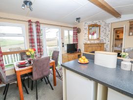A dining area with a table and chairs next to large windows and a kitchen counter with fruit and canisters visible at The Retreat Near Shorwell