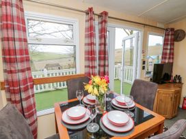 A dining area with a table set for four near windows and glass doors with red plaid curtains at The Retreat Near Shorwell