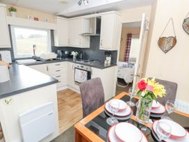 A kitchen with white cabinets and black countertops next to a dining table set with plates glasses and a vase of flowers at The Retreat Near Shorwell