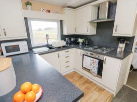 A kitchen with white cabinets a gas stove an oven a microwave a sink with a window above and oranges on a countertop at The Retreat Near Shorwell