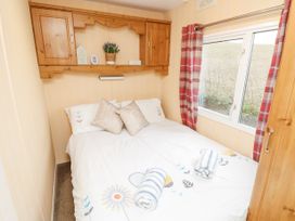 A bedroom with a double bed two rolled towels wooden cabinets and a window with red plaid curtains at The Retreat Near Shorwell