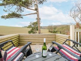 A deck with two reclining chairs around a table with a wine bottle and two glasses overlooking a field at The Retreat Near Shorwell
