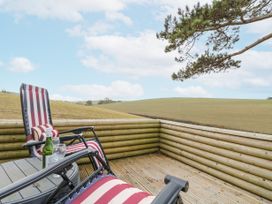 A wooden deck with striped chairs a bottle of wine and two glasses overlooking fields at The Retreat Near Shorwell