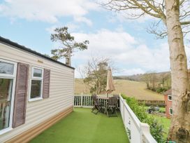 An outdoor deck with a round table and chairs next to a mobile home overlooking fields and trees at The Retreat Near Shorwell