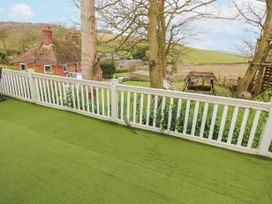 A terrace with green artificial grass flooring and white railing overlooking a garden with trees a wooden swing and a brick house in the background at The Retreat Near Shorwell