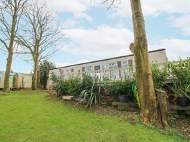 A mobile home with a white fence and plants in front of it with trees and a lawn at The Retreat Near Shorwell