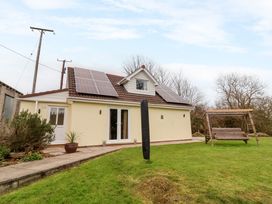 A house with solar panels on the roof and a wooden swing in the garden at Hideaway in Great Torrington