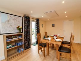 A dining room with a wooden table set for four and a bookshelf with books and games at Hideaway in Great Torrington