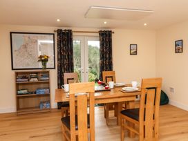 A dining room with a wooden table and chairs and a bookshelf with books and flowers at Hideaway in Great Torrington
