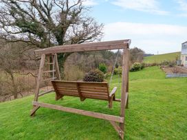 A wooden garden swing on a grassy lawn with trees and bushes in the background at Hideaway in Great Torrington
