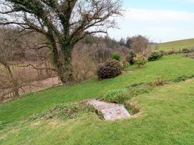 A grassy garden with steps leading down a hillside and bushes near a large tree at Hideaway in Great Torrington