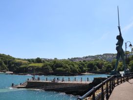 A metal statue holding a sword on a seaside promenade with a pier and houses on a hill in the background at Hideaway Great Torrington