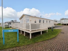 A white mobile home with a wraparound deck and a blue sign reading Beech on a grass lawn at Beech 20 in Cayton Bay