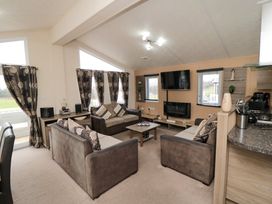 A living room with three sofas a coffee table a wall mounted TV and windows with curtains at Beech 20 in Cayton Bay