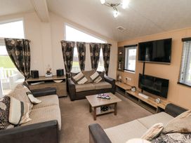 A living room with three sofas a coffee table curtains and a wall mounted television at Beech 20 in Cayton Bay