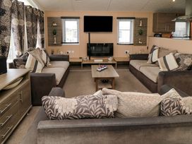 A living room with three sofas a coffee table a wall-mounted television and a fireplace at Beech 20 in Cayton Bay
