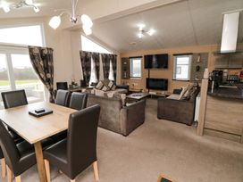 An open plan living room and dining area with a wooden table and leather chairs a sofa and armchairs a wall mounted television and windows with curtains at Beech 20 in Cayton Bay