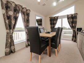 A dining area with a wooden table and six black chairs near windows with patterned curtains at Beech 20 in Cayton Bay