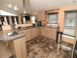 A kitchen with wooden cabinets a gas stove sink toaster and windows with blinds at Beech 20 in Cayton Bay