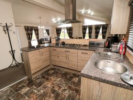 A kitchen with wooden cabinets a double sink and a stove next to a dining area with dark curtains at Beech 20 in Cayton Bay