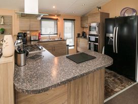 A kitchen with wood cabinets a black refrigerator a stove a sink and kitchen utensils at Beech 20 in Cayton Bay
