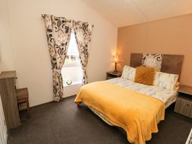 A bedroom with a bed covered by a yellow blanket and two bedside tables with lamps at Beech 20 in Cayton Bay