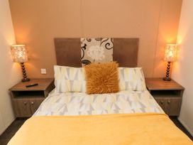 A bedroom with a double bed featuring patterned pillows and a yellow blanket beside two bedside tables with lit lamps at Beech 20 in Cayton Bay