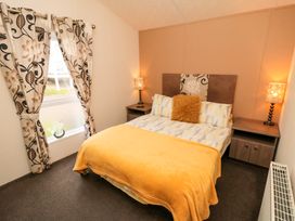A bedroom with a double bed two bedside tables with lamps patterned curtains and a window at Beech 20 in Cayton Bay