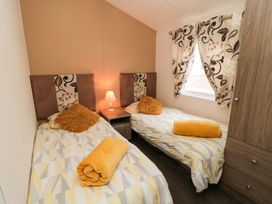 A bedroom with two single beds a nightstand with lamp a window with curtains and a wardrobe at Beech 20 in Cayton Bay