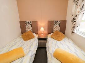 A bedroom with two single beds each with a yellow pillow and rolled towel a nightstand with a lamp between the beds and a window with patterned curtains at Beech 20 in Cayton Bay