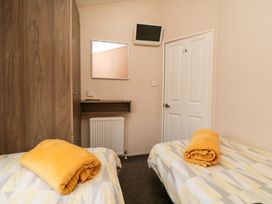 A bedroom with two single beds with yellow blankets on them a wall-mounted TV a wardrobe and a mirror at Beech 20 in Cayton Bay