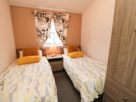 A bedroom with two single beds separated by a nightstand with a lamp and floral curtains on the window at Beech 20 in Cayton Bay