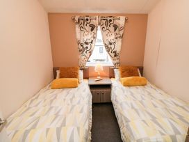 A bedroom with two single beds a nightstand lamp and patterned curtains at Beech 20 in Cayton Bay