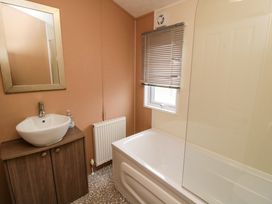 A bathroom with a sink on a wooden cabinet a mirror a bathtub with a glass screen a window with blinds and a radiator at Beech 20 in Cayton Bay