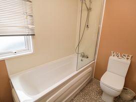A bathroom with a bathtub shower combination a window with blinds a toilet with a wash decoration and a small waste basket at Beech 20 in Cayton Bay
