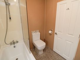 A bathroom with a bathtub shower, a toilet with the word wash on top, and a door with a hook at Beech 20 in Cayton Bay