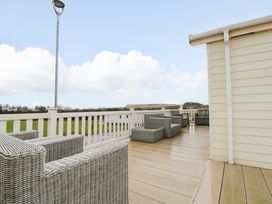 An outdoor wooden deck with wicker chairs and a white railing overlooking a grassy area at Beech 20 in Cayton Bay