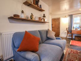 A living room showing a blue sofa with orange and beige cushions and wooden shelves with decorative items at Briar Orchard Annex Ammerham near Winsham