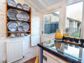 A kitchen with a wooden plate rack holding plates and mugs near a door and countertop with a yellow kettle and spice containers at Briar Orchard Annex in Ammerham near Winsham