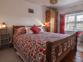 A bedroom with a wooden bed covered with floral bedding two pillows two bedside lanterns a wooden wardrobe a window with red curtains and a white chair at Briar Orchard Annex in Ammerham near Winsham