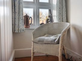 A white wicker chair with a cushion next to a window with floral curtains and decorative items on the windowsill at Briar Orchard Annex in Ammerham near Winsham