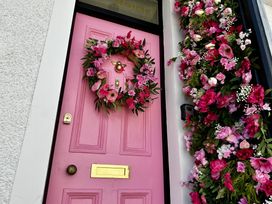 A pink front door with a floral wreath and pink flower decorations on the side at Ivy House in Conwy