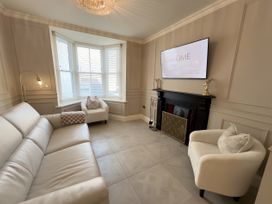 A living room with a leather sofa two armchairs a bay window a fireplace and a wall-mounted television at Ivy House in Conwy