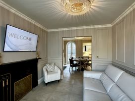 A sitting room with a white sofa armchair wall mounted tv and fireplace opening to a dining area at Ivy House in Conwy