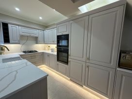 A kitchen with white cabinets and countertops a built in oven a gas stove and under cabinet lighting at Ivy House in Conwy