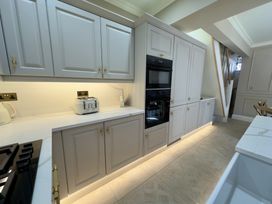 A kitchen with white cabinets and drawers a built in oven a white toaster and kettle a white countertop and wooden chairs at Ivy House Conwy