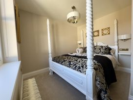 A bedroom with a four-poster bed with patterned bedding a chandelier and framed wall art at Ivy House in Conwy