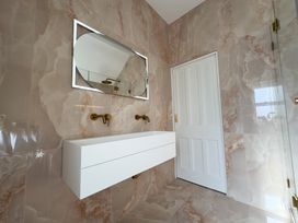 A bathroom with a white floating sink cabinet two wall-mounted faucets an oval mirror with a light and a white door at Ivy House in Conwy